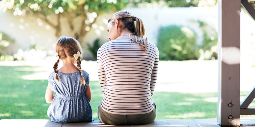 A woman and small girl sitting together on a porch, talking.