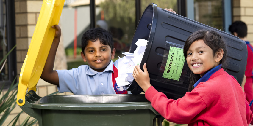 Two students from South Coogee Primary School tipping a recycling collection bin into a kerbside recycling bin.